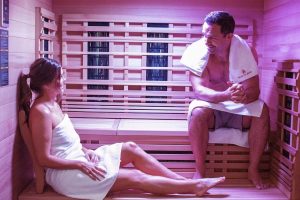 A young man and woman sitting and relaxing in an infrared sauna with candles.