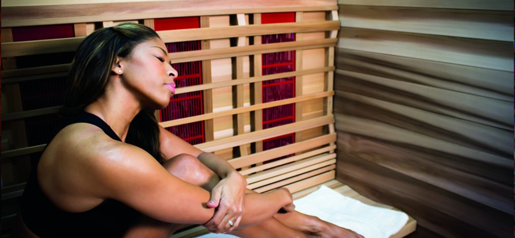 young woman enjoys a session in her infrared sauna while using a towel to absorb perspiration