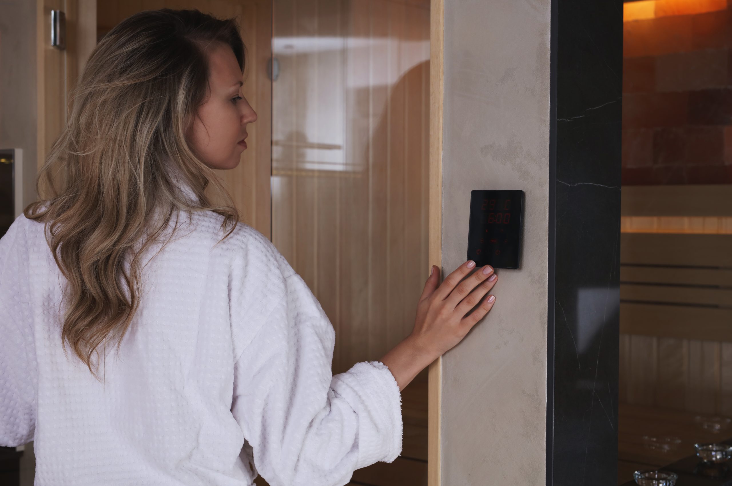 A woman in a white bathrobe adjusts the electronic temperature adjuster on her in-home infrared sauna before entering.